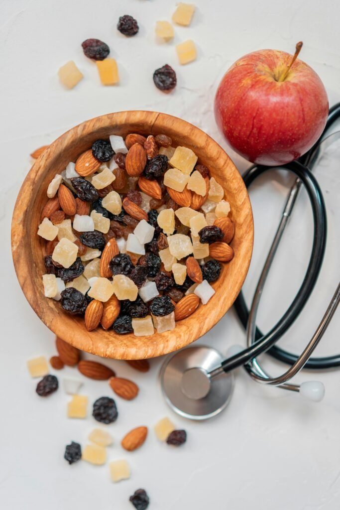 Top view of a healthy mix of nuts and dried fruits with an apple and stethoscope.